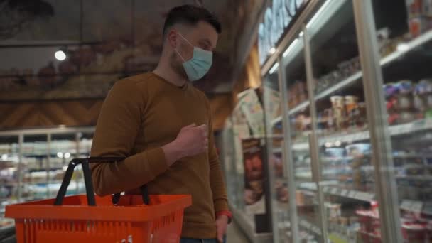 Salud, compras de seguridad y concepto de pandemia. Hombre cliente en máscara comprando comida en el supermercado. Protección y prevención de medidas. Hombre joven en la cara de la máscara de compras en el supermercado con carro. Covid 19 — Vídeo de stock