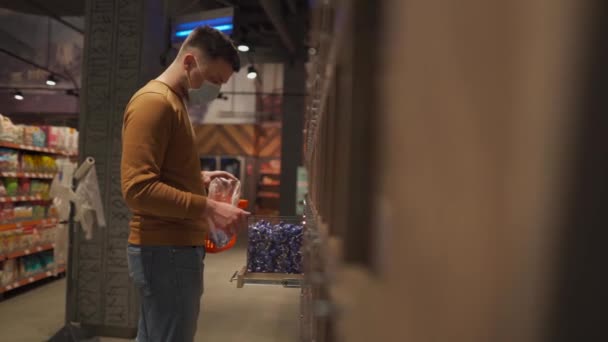 Salud, compras de seguridad y concepto de pandemia. Hombre cliente en máscara comprando comida en el supermercado. Protección y prevención de medidas. Hombre joven en la cara de la máscara de compras en el supermercado con carro. Covid 19 — Vídeos de Stock