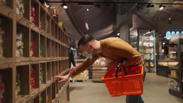 Giovane uomo caucasico in maschera che sceglie latticini al supermercato durante la pandemia coronavirus. Shopping maschile al supermercato indossando maschera facciale, carrello della spesa in mano. Argomento nuova norma covid 19 — Video Stock