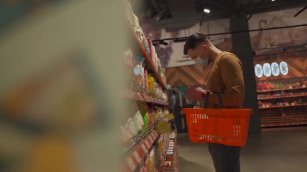 Hälsa, säkerhet och pandemi. Man klient i mask köper mat i mataffären. Skydd och förebyggande åtgärder. Ung man i ansiktet mask shopping i snabbköpet med vagn. Avdelning 19 — Stockvideo