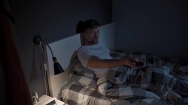 Depresyon ve uykusuzluktan muzdarip beyaz bir adam TV izlerken kendini eğlendirmeye çalışıyor, geceleri uzaktan kumandayla kanal değiştiriyor.