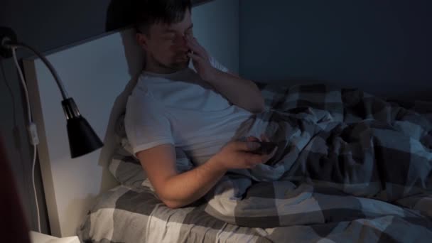 Unavený muž drží v rukou dálkové ovládání televizoru, usíná a v noci se dívá na televizi v posteli. Tématická závislost na streamovacích službách, filmech a televizních pořadech. Muž trpí v noci nespavostí — Stock video