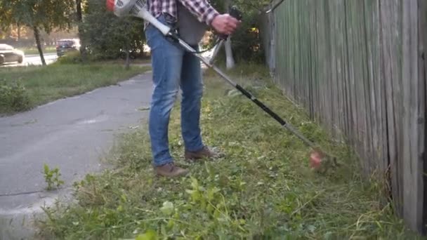 Professioneel maaien langs de weg. Bouw medewerker met borstel maaien voor het verwijderen van gras. Tuinman maait onkruid. Man met benzinemaaier. Werknemer in overall maait gras op gazon met trimmer in de buurt van de rijbaan — Stockvideo