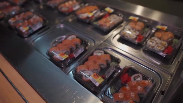Hombre caucásico con máscara protectora en la cara elige el conjunto de sushi en caja para ir en el supermercado durante la cuarentena y la epidemia de coronavirus. Comida japonesa para llevar. Comida saludable, lonchera — Vídeo de stock