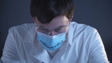 Genç doktor çok yorgun ve kovid 19 ile enfekte olmuş, üzgün, elleriyle başını kaldırmış, maske koronavirüs üzerine yazılmış sözlerle kafasını maskesine kaldırmış. Salgın sırasında tıbbi sistem çökmesi