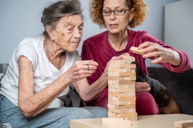 Emekli anne ve kızı evde birlikte vakit geçirir, masa oyunu oynar ve dachshund köpeği okşarlar. Kafkas kıdemli kadın bakım evinde gönüllü asistanı olan ahşap bloklardan bir kule inşa ediyor..