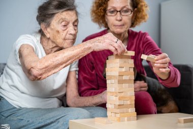 Emekli anne ve kızı evde birlikte vakit geçirir, masa oyunu oynar ve dachshund köpeği okşarlar. Kafkas kıdemli kadın bakım evinde gönüllü asistanı olan ahşap bloklardan bir kule inşa ediyor..
