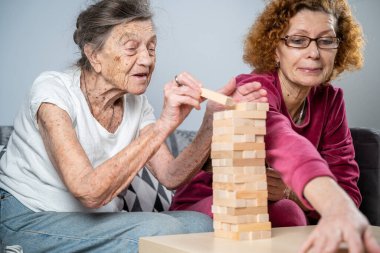 Emekli anne ve kızı evde birlikte vakit geçirir, masa oyunu oynar ve dachshund köpeği okşarlar. Kafkas kıdemli kadın bakım evinde gönüllü asistanı olan ahşap bloklardan bir kule inşa ediyor..