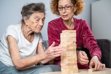 Emekli anne ve kızı evde birlikte vakit geçirir, masa oyunu oynar ve dachshund köpeği okşarlar. Kafkas kıdemli kadın bakım evinde gönüllü asistanı olan ahşap bloklardan bir kule inşa ediyor..
