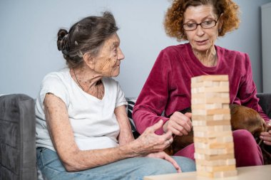 Emekli anne ve kızı evde birlikte vakit geçirir, masa oyunu oynar ve dachshund köpeği okşarlar. Kafkas kıdemli kadın bakım evinde gönüllü asistanı olan ahşap bloklardan bir kule inşa ediyor..