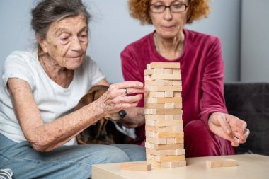 Emekli anne ve kızı evde birlikte vakit geçirir, masa oyunu oynar ve dachshund köpeği okşarlar. Kafkas kıdemli kadın bakım evinde gönüllü asistanı olan ahşap bloklardan bir kule inşa ediyor..