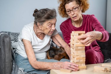 Emekli anne ve kızı evde birlikte vakit geçirir, masa oyunu oynar ve dachshund köpeği okşarlar. Kafkas kıdemli kadın bakım evinde gönüllü asistanı olan ahşap bloklardan bir kule inşa ediyor..