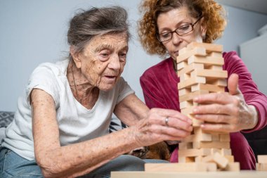 Emekli anne ve kızı evde birlikte vakit geçirir, masa oyunu oynar ve dachshund köpeği okşarlar. Kafkas kıdemli kadın bakım evinde gönüllü asistanı olan ahşap bloklardan bir kule inşa ediyor..