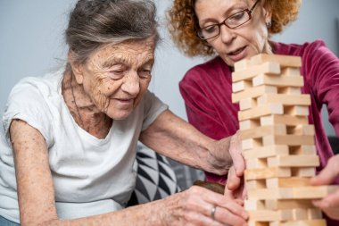 Emekli anne ve kızı evde birlikte vakit geçirir, masa oyunu oynar ve dachshund köpeği okşarlar. Kafkas kıdemli kadın bakım evinde gönüllü asistanı olan ahşap bloklardan bir kule inşa ediyor..