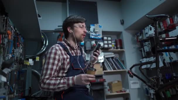 Relaxation while working, having fun in workplace by listening to music and drinking coffee. Man who loves his profession. Bicycle mechanic fun listening music, enjoy song, excited lifestyle concept — Stock Video