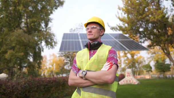 代替エネルギーの概念。保護制服と太陽電池パネルの近くにポーズ黄色のハード帽子の若い誇り高い労働者。持続可能なクリーンエネルギー。太陽光発電所と幸せな手水舎の肖像 — ストック動画