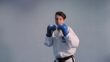 Siyah kuşaklı beyaz kimonolu karate ve tekvando kadın. Trenler mavi spor eldivenlerini yumrukluyor ve tekmeliyor. Dövüş sanatları yapan kadın dövüşçü. Tekvando oyuncusu alıştırması. Ukrayna, Kiev 20 Mart 2017