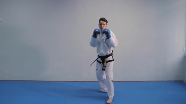 Vrouw en vechtsport thema voor zelfverdediging oefenen van een paar trucs. Vrouwelijke taekwondo vechter in witte kimono, zwarte riem en blauwe handschoenen traint schaduwboksen in de sportschool. Oekraïne, Kiev 20 maart 2017 — Stockvideo