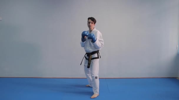 Mujer de karate y taekwondo en kimono blanco con cinturones negros entrena golpes y patadas en guantes deportivos azules. Peleadora haciendo artes marciales. Prácticas de jugador de Taekwondo. Ucrania, Kiev marzo 20, 2017 — Vídeos de Stock