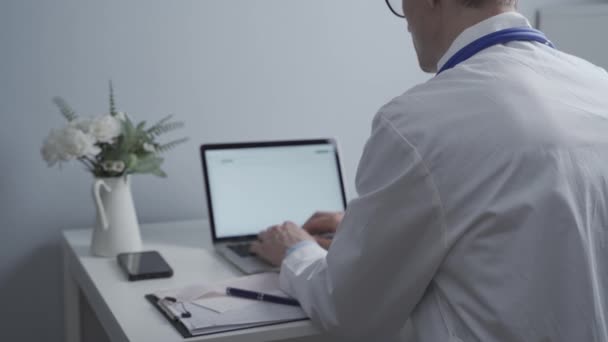 在医院工作的年轻医生，使用笔记本电脑，输入回放视图。医学、专业、技术和人的概念。Coronavirus, covid-19.从事医疗图表和文件工作的医生 — 图库视频影像