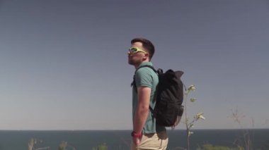 Kafkas erkek turist güneşli yaz havasında dağ yolunda haikin yaparken deniz manzarası seyrediyor. Lycian yolunda yürüyüş. Sırt çantalı gezgin uçurumun kenarında duruyor. Macera, seyahat insanları konsepti