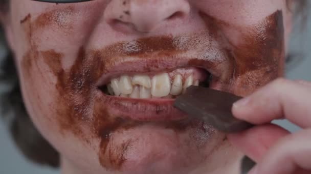Beyaz kadın tatlıya düşkündür ve diş sorunları vardır. Stüdyoda yüzü çikolata kaplı, çenesi dişleri ve fiber iğnesi olan bir kadın. Dişler için kötü alışkanlıklar. Zararlı yiyecekler. Ön dişi kırılmış. — Stok video