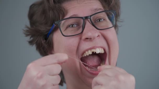 Sława z zepsutymi zębami zmieniła zdanie późno i używa nici dentystycznej, ale za późno ma uszkodzone zęby. Kobieta z uszkodzonym przednim zębem sprawia, że higiena jamy ustnej na szarym tle. Opieka zdrowotna — Wideo stockowe