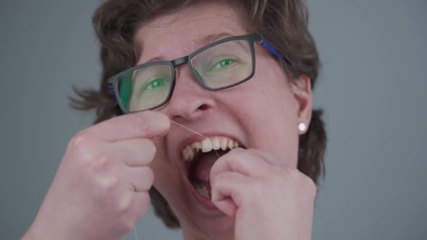 Famale with bad teeth changed her mind late and uses dental floss, but too late her teeth are damaged. Woman with damaged front tooth makes oral hygiene on gray background. Healthcare — Stock Video