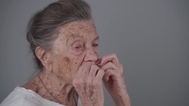 Probleem met tanden op hoge leeftijd. Senior vrouw paste kunstgebit in studio op grijze achtergrond. Oudere vrouw met grijs haar en diepe rimpels 90 jaar oude inserts valse tanden. Oma gebruik tandprothese — Stockvideo