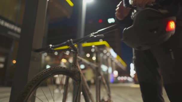 Ciudad ciclismo tema de seguridad. El repartidor se pone el casco con luz roja antes de andar en bicicleta por las calles nocturnas de la ciudad. Paseo masculino a casa después del trabajo en bicicleta por la noche y se pone el casco. Protección del ciclo — Vídeo de stock