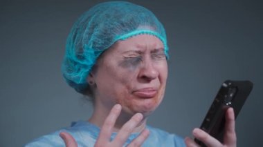 Tek kullanımlık mavi koruyucu elbisesi olan kadın ağlıyor ve acil servisteki sigorta şirketini arıyor. Klinikte şiddetin ardından yüz yaralanması geçiren bir kadın sosyal hizmetleri aramış.