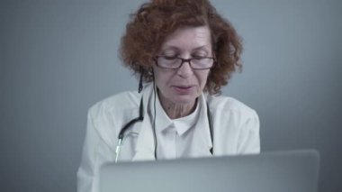 Orta yaşlı kadın pratisyen hekimin iş arkadaşlarıyla görüntülü görüşmesi var. Doktor sanal sağlık randevusu sırasında hastayla konuşuyor. Bilgisayardaki internet kamerasından doktorların konuşması
