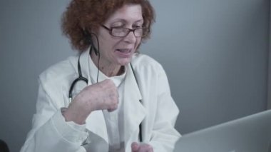 Orta yaşlı kadın pratisyen hekimin iş arkadaşlarıyla görüntülü görüşmesi var. Doktor sanal sağlık randevusu sırasında hastayla konuşuyor. Bilgisayardaki internet kamerasından doktorların konuşması