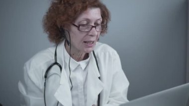 Çevrimiçi tıbbi tedavi uygulayan kadın sağlık çalışanı. Tıbbi asistan bilgisayardan uzak hastayı ararken kulaklık takıyor. Teletıp konsepti. Çevrimiçi doktor randevu uygulaması sanal toplantı