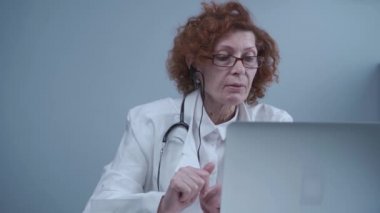 Orta yaşlı kadın pratisyen hekimin iş arkadaşlarıyla görüntülü görüşmesi var. Doktor sanal sağlık randevusu sırasında hastayla konuşuyor. Bilgisayardaki internet kamerasından doktorların konuşması