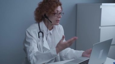 Teletıp hizmetleri. Ana bakım konsültasyonları, psikoterapi, acil servisler. Bilgisayarda online danışmanlık yaparken konuşan ve el kol hareketi yapan bir kadın doktor. Tıp, sağlık hizmeti kavramı