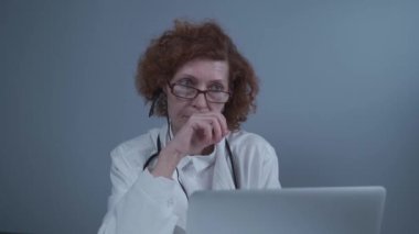 Çevrimiçi tıbbi tedavi uygulayan kadın sağlık çalışanı. Tıbbi asistan bilgisayardan uzak hastayı ararken kulaklık takıyor. Teletıp konsepti. Çevrimiçi doktor randevu uygulaması sanal toplantı