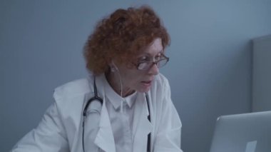 Orta yaşlı kadın pratisyen hekimin iş arkadaşlarıyla görüntülü görüşmesi var. Doktor sanal sağlık randevusu sırasında hastayla konuşuyor. Bilgisayardaki internet kamerasından doktorların konuşması