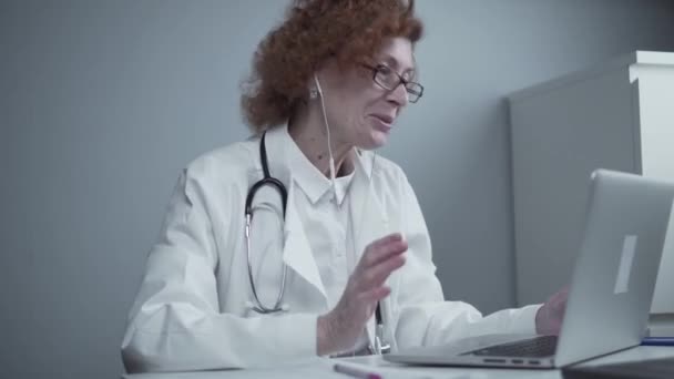 Servizi di telemedicina. Consulenze primarie, psicoterapia, servizi di emergenza. Medico donna parlando e gesticolando pur avendo consultazione online sul computer portatile. Medicina, concetto di assistenza sanitaria — Video Stock