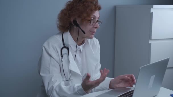 Médico general mujer de mediana edad tienen videollamada con colegas en la oficina. Doctor hablando con el paciente durante la cita médica virtual. Médico hablar por webcam en línea videollamada en el ordenador portátil — Vídeo de stock