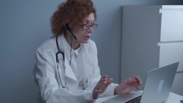 Kvinnlig hälso- och sjukvårdspersonal som ger medicinsk behandling online. Medicinsk assistent bär hörlurar video samtal avlägsen patient på laptop. Telemedicinskt koncept. Online läkarbesök app virtuellt möte — Stockvideo