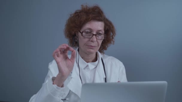 Média idade mulher generalista têm videochamada com colegas no escritório. Médico conversando com paciente durante consulta médica virtual. Conversa médica por webcam on-line chamada de vídeo no laptop — Vídeo de Stock