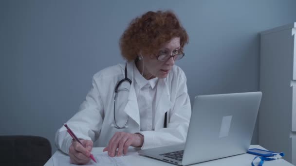 Női egészségügyi dolgozó, aki online orvosi ellátást nyújt. Orvosi asszisztens hord headset video hívás távoli beteg laptopon. Telemedicina koncepció. Online orvosi kinevezés alkalmazás virtuális találkozó — Stock videók