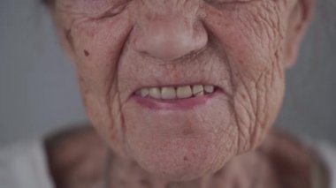 Yakından mutlu, Kafkas kıdemli bir kadın kameraya bakıyor ve gri arka planda gülüyor. Stüdyoda mutlu 90 yaşındaki bir büyükannenin portresi. Yaşlılar için takma diş