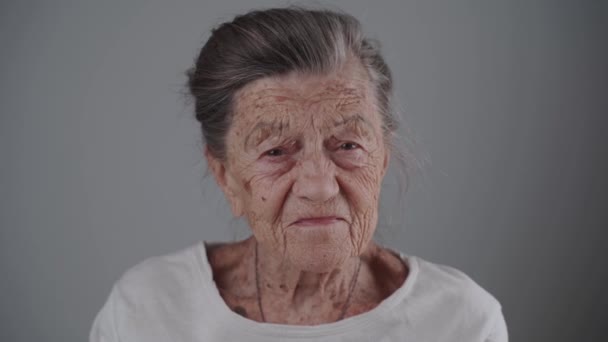 Ritratto di donna caucasica felice con sorriso su sfondo grigio in studio. Primo piano di una vecchia donna di 90 anni con i capelli grigi e le rughe profonde che sorridono guardando nella fotocamera. Anziani attivi — Video Stock