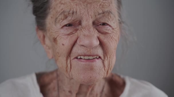 Ritratto di donna caucasica felice con sorriso su sfondo grigio in studio. Primo piano di una vecchia donna di 90 anni con i capelli grigi e le rughe profonde che sorridono guardando nella fotocamera. Anziani attivi — Video Stock