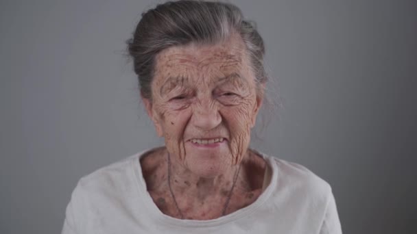 Усміхнена літня старша леді з зубним протезом в студії на сірому фоні. Позитивність і довголіття. Пенсійне почуття задоволене. Ти ніколи не старий, щоб бути щасливим. Весела літня жінка сміється — стокове відео