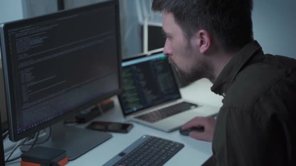 Programování. Muž pracující na počítači v IT sedí u pracovního stolu s PC a notebookem, píše kódy. Programátor zadává datový kód, pracuje na projektu v softwarové vývojářské společnosti. Vývojář IT — Stock video