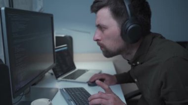 Tecritteyken akıllı çalışma kavramı. Kulaklık takan programcı, ofisteki bilgisayar başında oturuyor. Kodlama, programlama. Yeni proje için programlama kodu üzerinde çalışan yazılım mühendisi