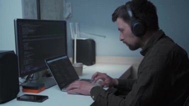 Tecritteyken akıllı çalışma kavramı. Kulaklık takan programcı, ofisteki bilgisayar başında oturuyor. Kodlama, programlama. Yeni proje için programlama kodu üzerinde çalışan yazılım mühendisi